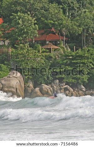 A surfer enjoys the warm water waves at an Idyllic beach in Phuket, backed by lush rainforest