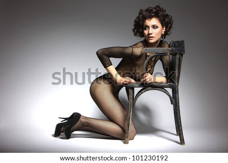 Sexy glamor model girl posing in black belei shoes with heels, kneeling beside the chair in retro style