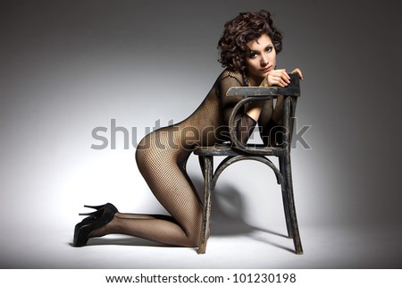 Sexy glamor model girl posing in black belei shoes with heels, kneeling beside the chair in retro style