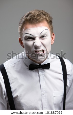 A person close-up of mime, the emotion of aggression, a black bow tie, theatrical makeup, isolated on a gray background