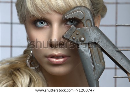 Sexy blonde poses with pliers against the steel mesh in the studio