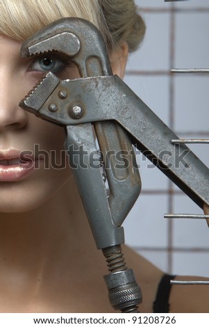 Sexy blonde poses with pliers against the steel mesh in the studio