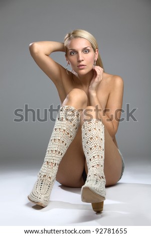 A beautiful Woman wearing knee length boots seated on the studio floor with her long leg concealing her breasts, implied topless.