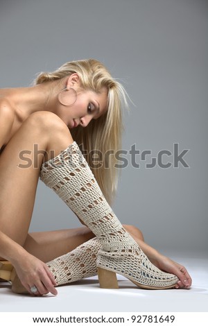 A beautiful Woman wearing knee length boots seated on the studio floor with her long leg concealing her breasts, implied topless.