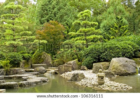A tranquil scene with rocks, a rock lantern, water and trees in a japanese garden