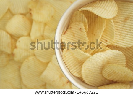 closeup top shot potato chips in white bowl with potato chip background.