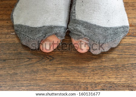 worn out socks with a hole and toes sticking out  of them on  old wooden floor .