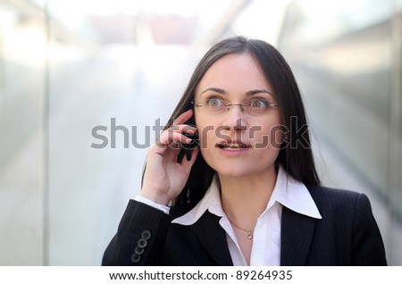A surprised business woman is talking on the phone in front of a corporate building.