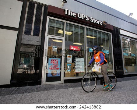 NEW YORK CITY - MONDAY, DEC. 29, 2014: A bicycle messenger rides by a UPS Store. The UPS Store network is the world\'s largest franchisor of retail shipping, postal,  and business service centers