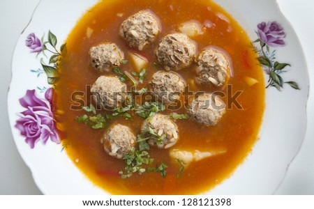 A tomato soup with meatballs on a plate with flowers