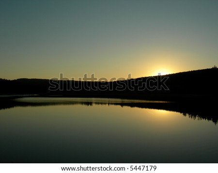 Sun is setting behind forest an is mirroring in the lake