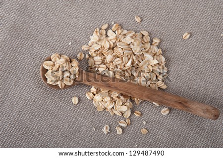 Pile of oat on a beige table cloth with a wooden spoon