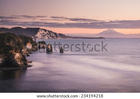 sunset over sea shore rocks and mount Taranaki New Zealand