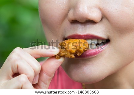 The mouth of a woman is eating fried chicken pieces.