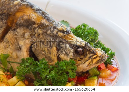Snapper fish topped with chili sauce on a white plate.