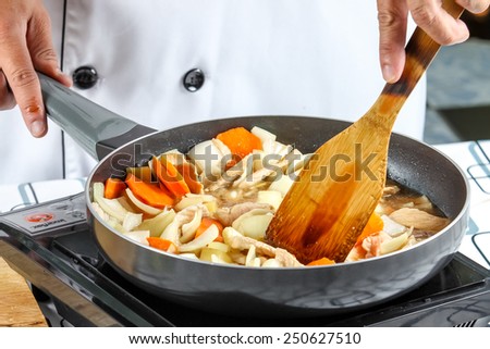 chef cooking stir fry vegetables with pork in outdoor kitchen