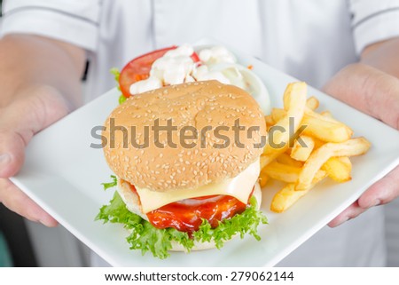 chef holding american cheese burger with fresh salad and french fries