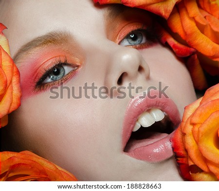 the beautiful girl model with shining skin with a saturated bright make-up in flowers, fiery color
