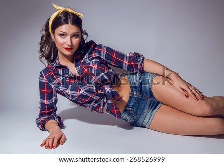 model in the style of pin-up, beauty, beauty with dark hair, a girl with a beautiful figure, in short shorts and a plaid shirt, with heels on a light background
