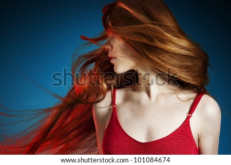 Sexy young red hair woman in red dress on dark blue background