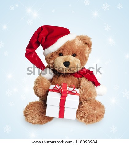 Cute toy bear with christmas gift and santa hat on light background