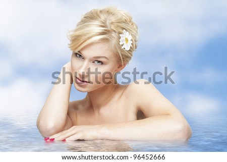 Young blond woman with daisy in hair in water on blue sky