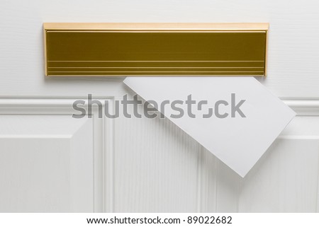 Blank envelope posted through copper letter box in white door