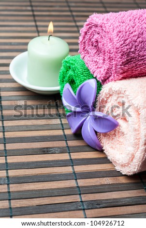 Spa towels rolls, flower and burning candle lying on wooden mat. Vertical composition.
