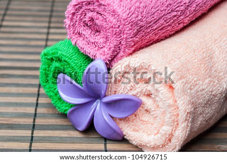 Closeup spa towels rolls and flower lying on wooden mat. Horizontal composition.