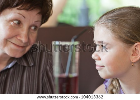 Senior woman and her granddaughter smiling to each other in open-air restaurant in a park