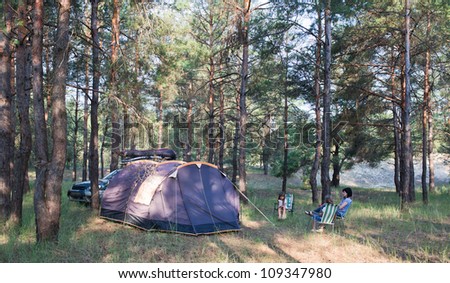 Camping at pine forest. Black tent, car with equipment. Family resting outdoors