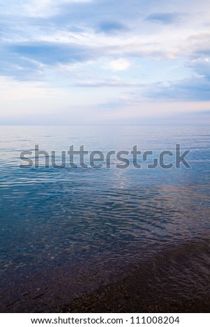 Sky mirroring on the sea to the horizon. Cloudy blue sky close to sunset