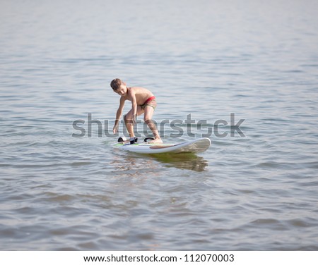 Young boy practicing surfing moves on a surfboard on water