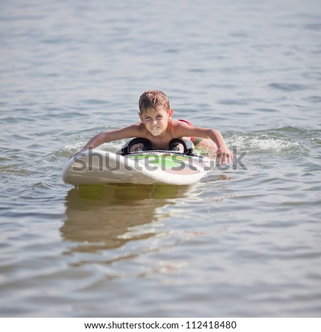 Young boy practicing surfing moves on windsurfing board on water