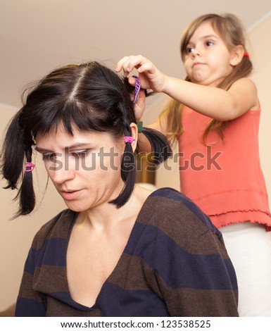 Cute little girl making her mother funny haircut