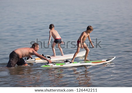 A two caucasian little boys are learning how to surf and are getting a lesson from a male instructor