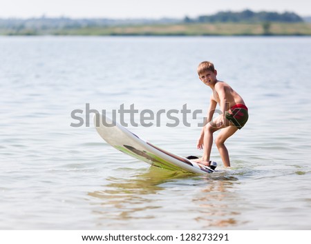Young boy practicing surfing moves on a surfboard on water
