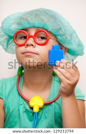 Cute little girl with toy glasses and a doctor\'s costume holds a toy stethoscope and toy bottle of medicine