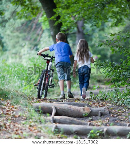 Children walking  in forest.  Llittle boy walking with his bike high up