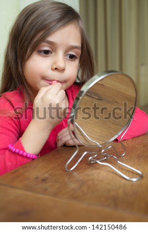 Little girl making makeup in front of small mirror