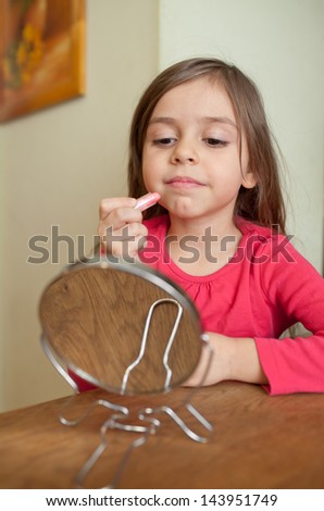Little girl doing makeup in front of small mirror