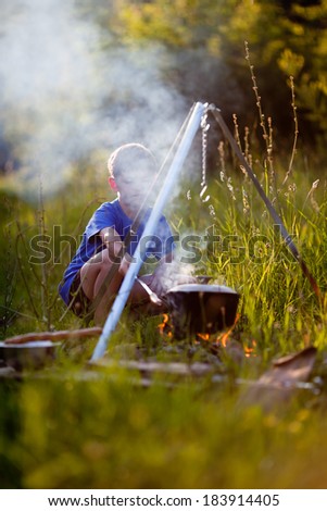 Little boy cooks on a fire in wild camping. The smoke