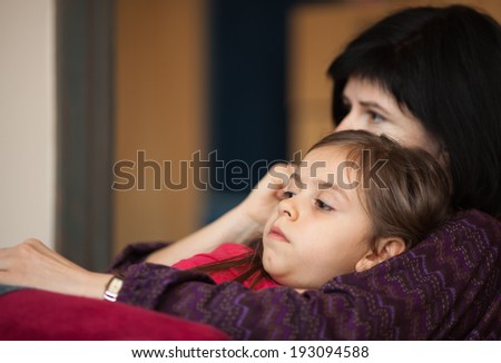 Little girl and her mother looking something interesting on TV sitting on sofa