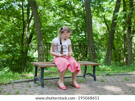 The girl and birdie (titmouse) sitting on a bench in a park. Girl looking at bird