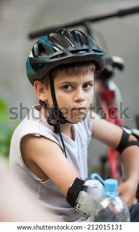 A cute boy during a relax after sport training, wearing a bicycle helmet and protection