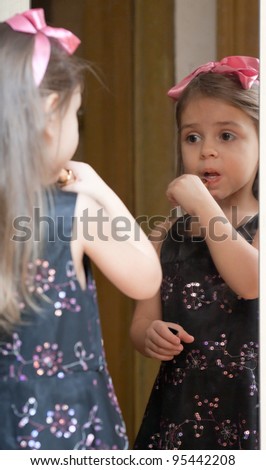 Fashionable little girl in black dress with pink bow paints her lips. Reflection in the mirror.