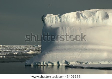 An Antarctic iceberg in the Southern Ocean on a nearly flat sea covered by ice floes. The iceberg is enlightened by the evening sun. Picture was taken during a 3-month research expedition.