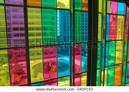 The picture shows a horizontal view through a coloured window front. City architecture behind the window gains a cubistically coloured aspect, contrasted by a rondell.