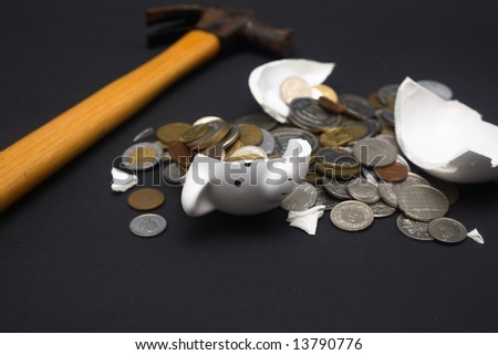 A broken piggy bank isolated on a dark background with loads of coins from around the world and a hammer.