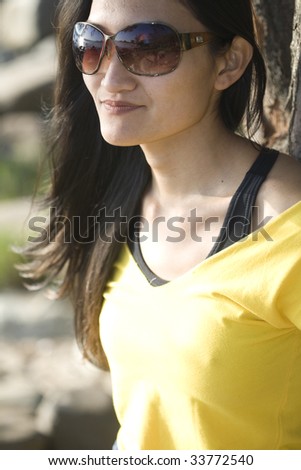 A brunette asian woman wearing a yellow tank top and sunglasses.